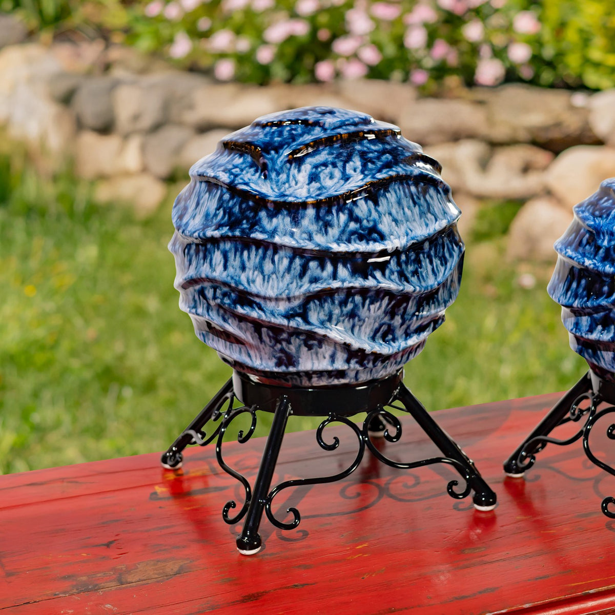 Blue-and-white ridged gazing globe on a black scrollwork stand, with part of another globe visible.