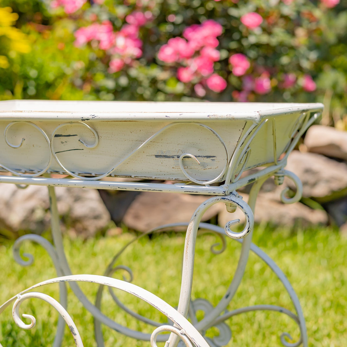 Close view of the pale metal cart tray and curled frame details against a flower-filled garden.