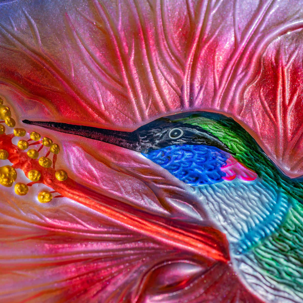 Close-up of a colorful hummingbird motif with a long beak against a pink, rippled glass bowl.