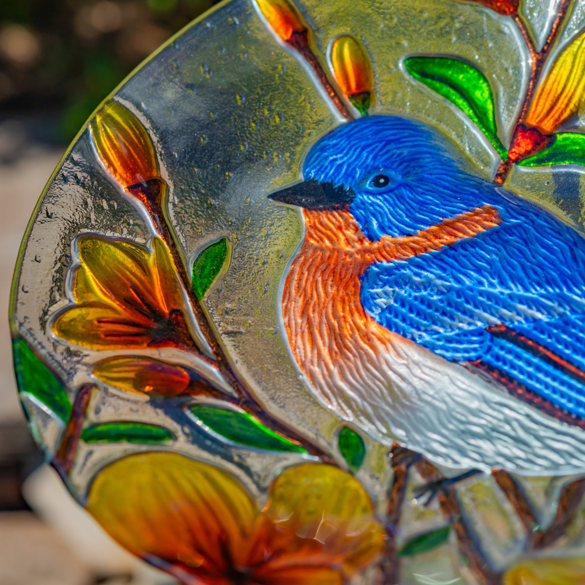 Close-up of a bluebird and colorful flowers embossed in a glass birdbath bowl.