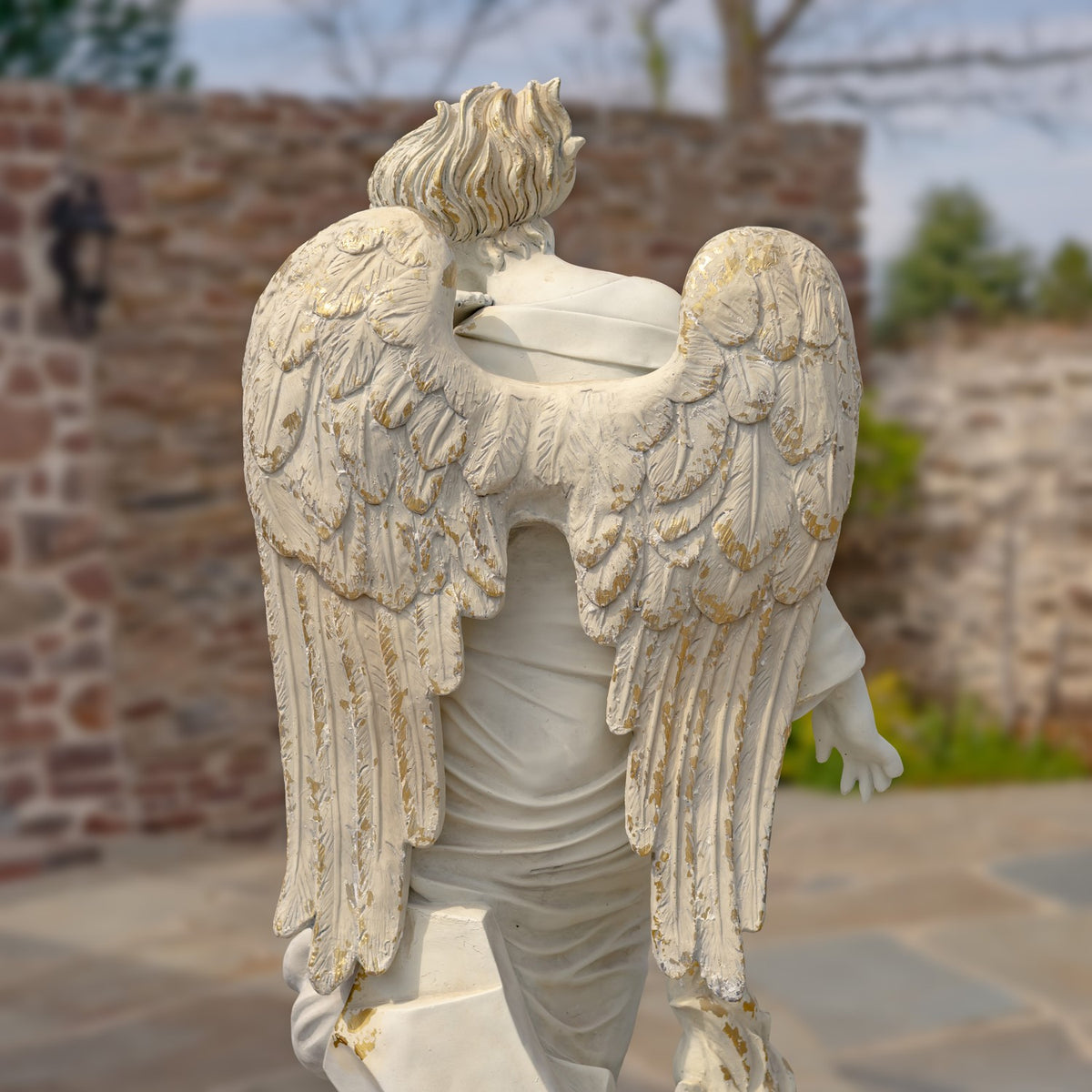 Rear view of a pale angel statue showing its layered wings and draped robe.