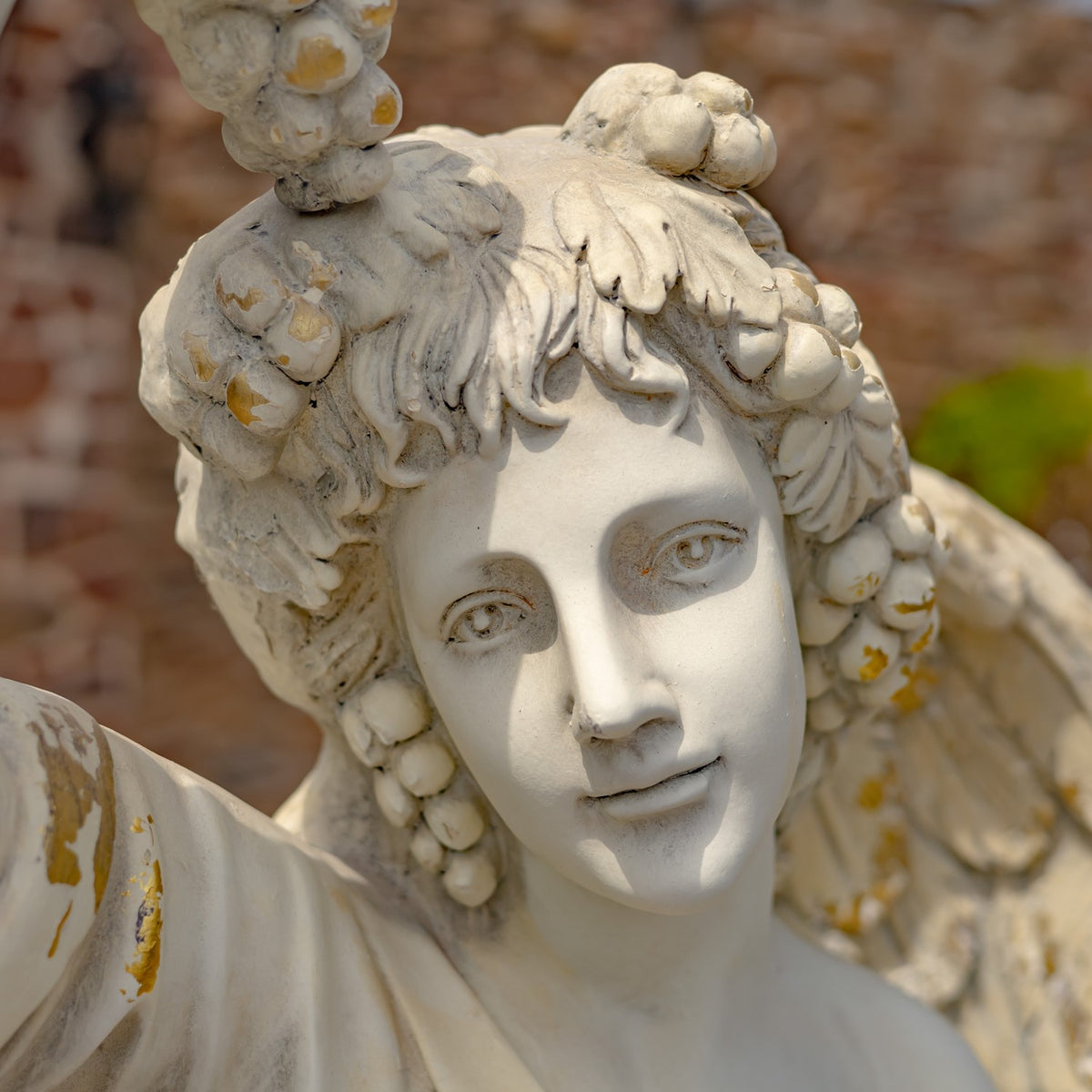 Close-up of the angel statue’s face, curled hair, and raised grapes.