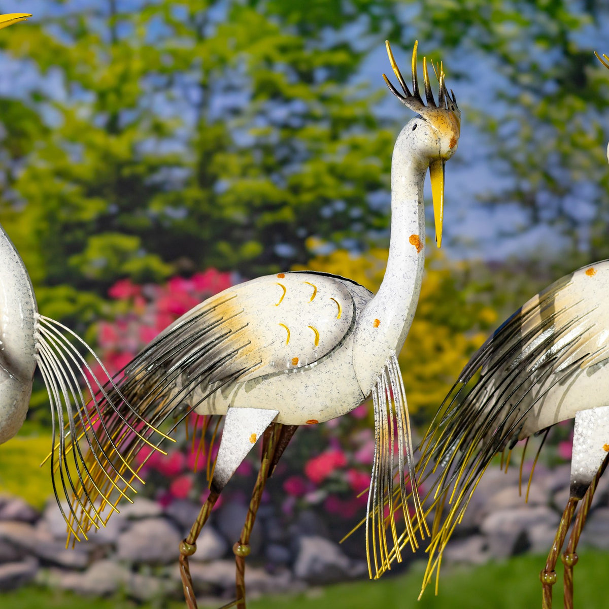 Close view of white metal heron figurines with long gold legs, slender feather details, and orange accents.