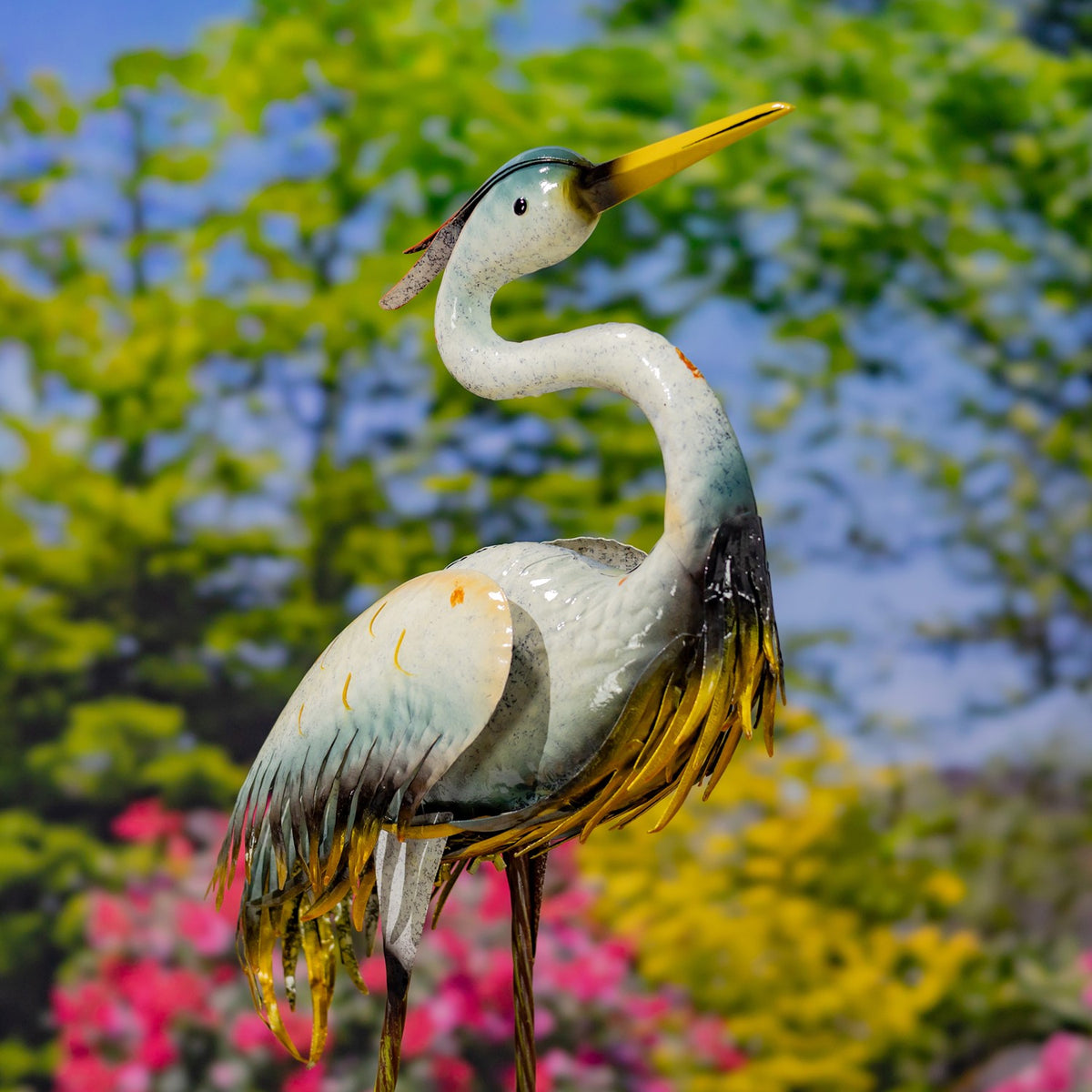 Metal crane garden figurine with a curved neck, yellow beak, and layered feather details against greenery.