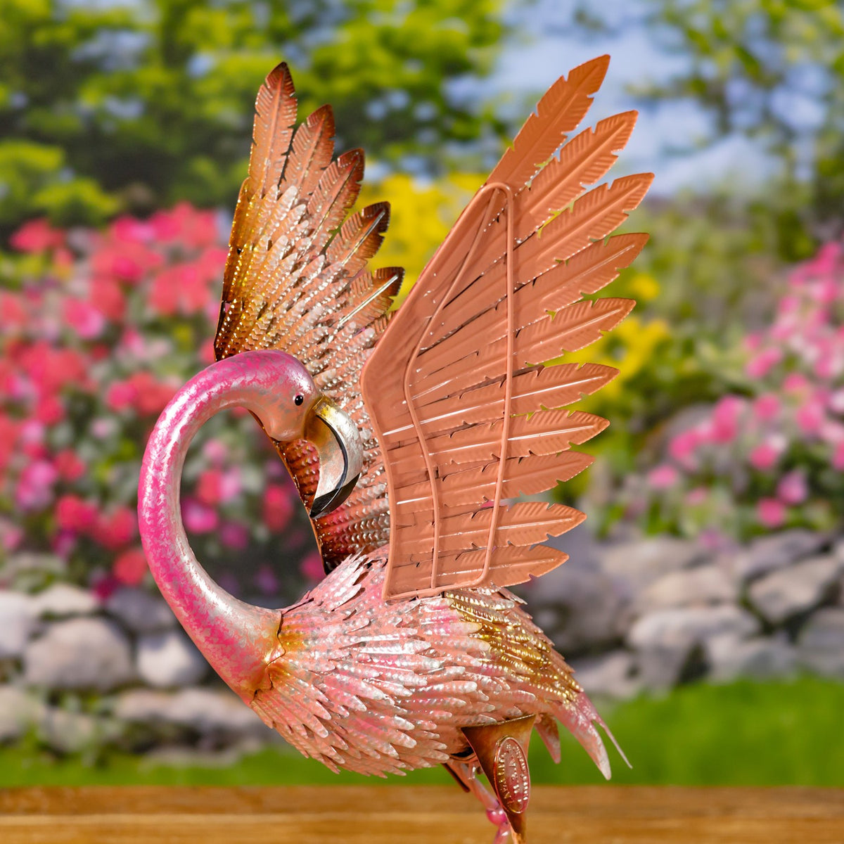 Close view of a pink metal flamingo with raised feathered wings and a curved neck.