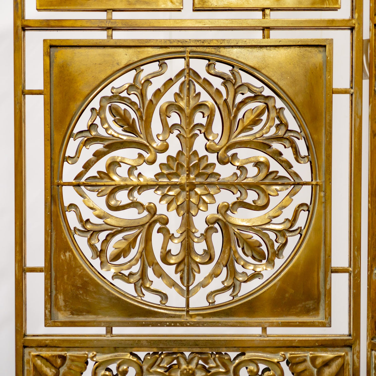 Close-up of a gold screen panel with a circular, symmetrical floral scrollwork design.