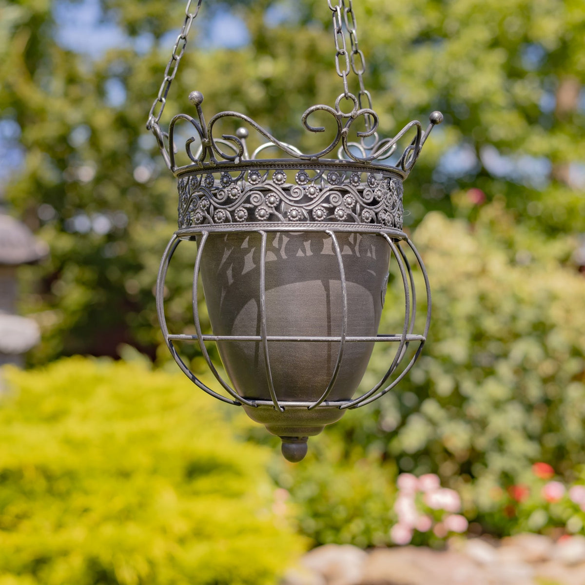 A hanging metal basket planter seen from a slight angle, with curved bars around its inner pot.