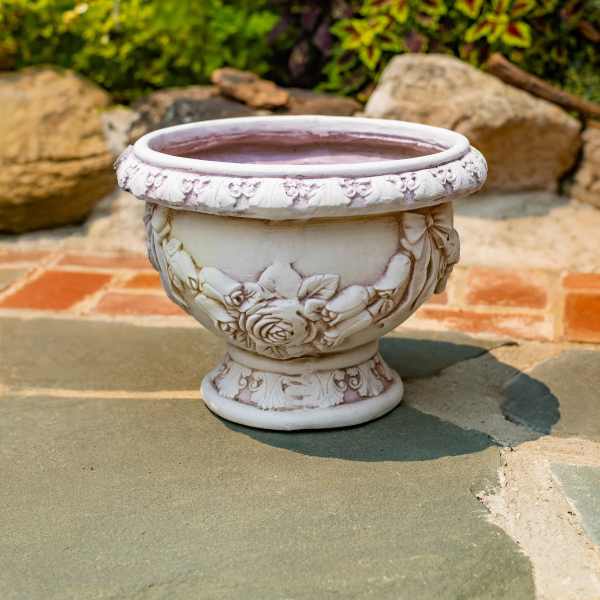 Antique-white pedestal flower pot with raised floral decoration on a stone patio.