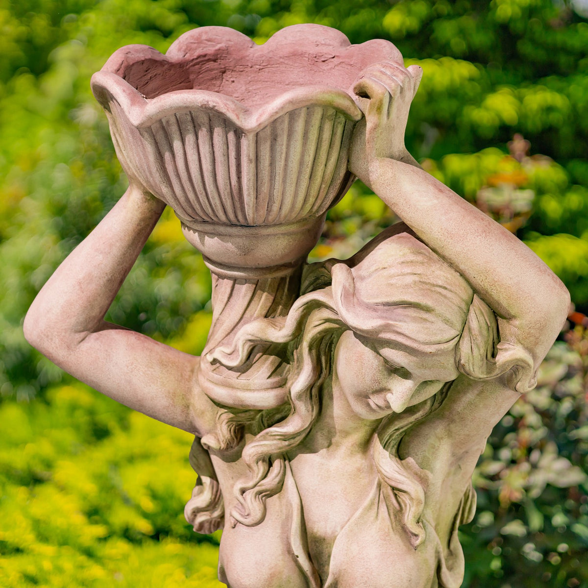 Close view of a carved woman holding a large fluted flower pot above her head.