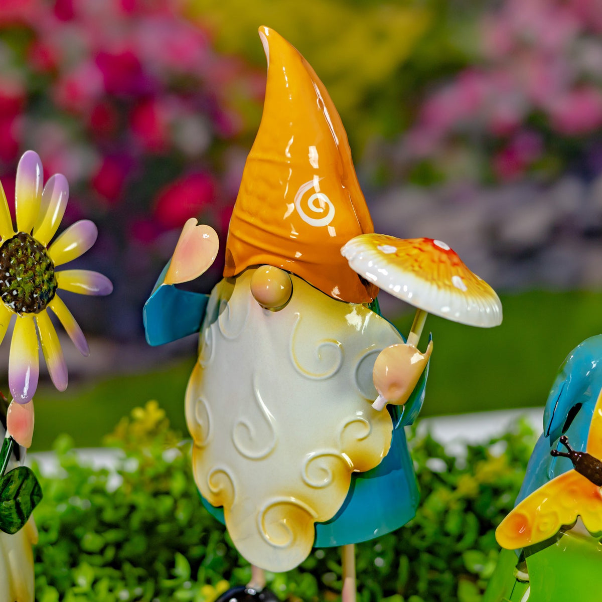 Close view of a white-bearded garden gnome in an orange hat beside a mushroom and flower stakes.