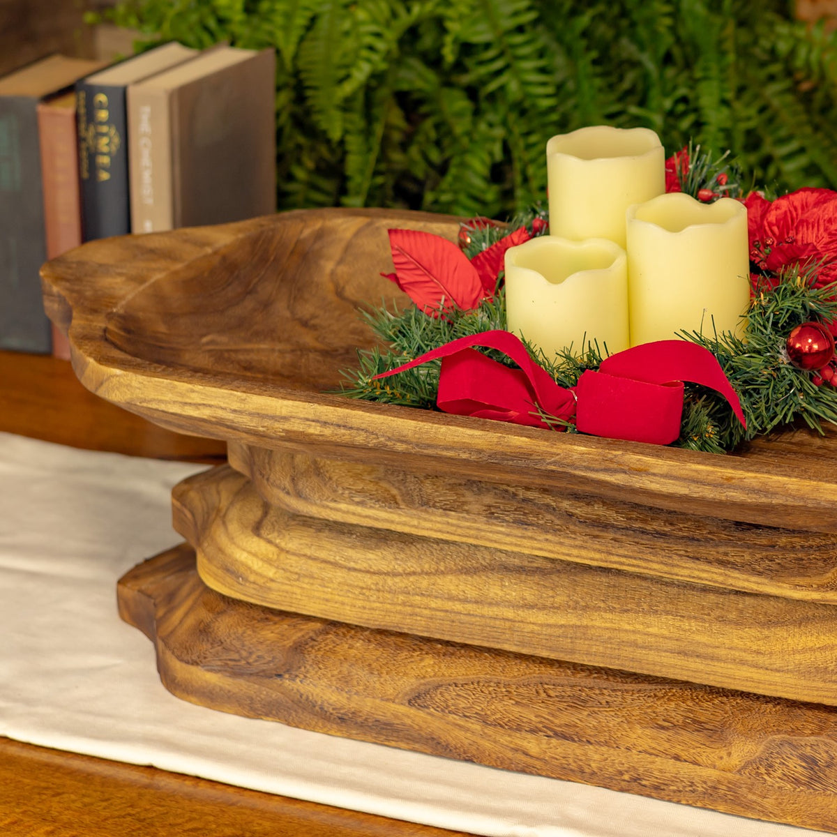Close view of a wooden tray holding candles and red holiday greenery.