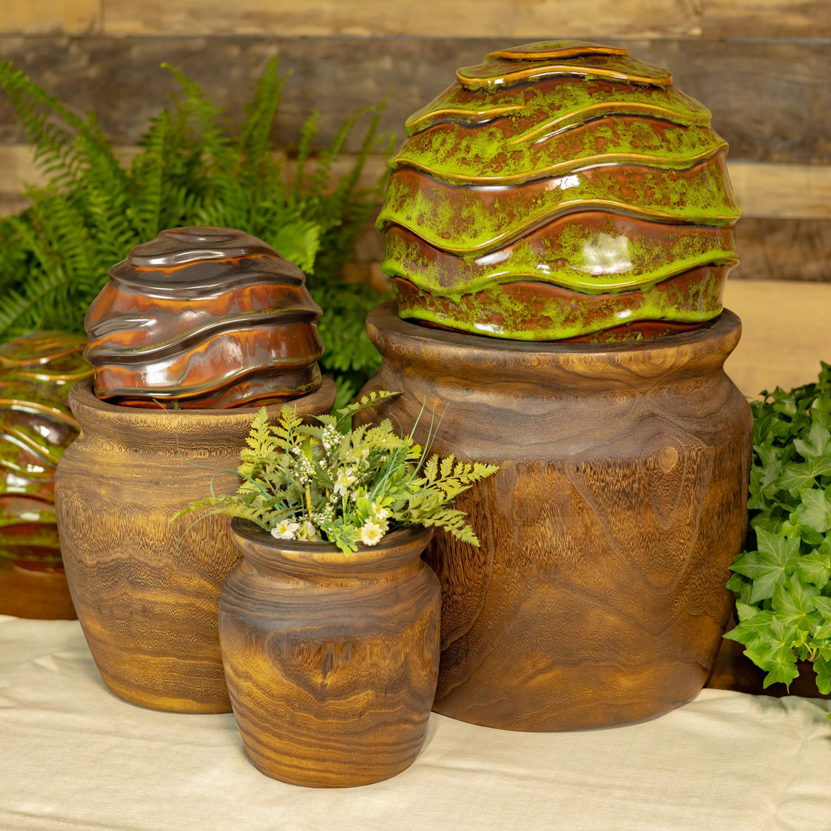 Three round wooden planters grouped together, with two decorative lidded pots and greenery.