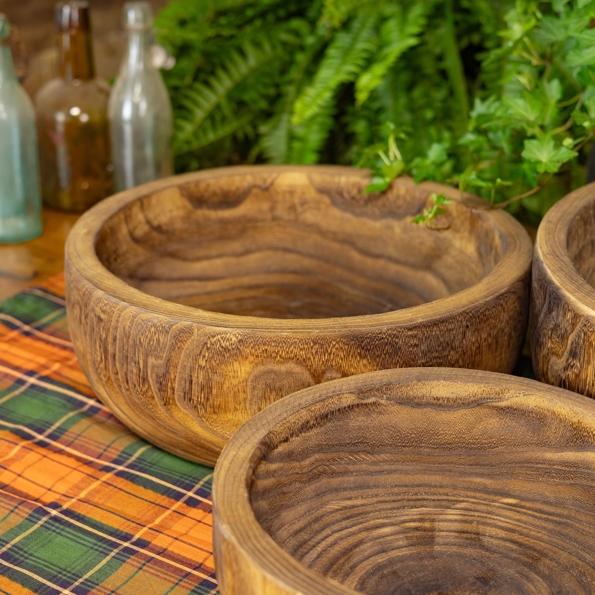 Close view of rustic round wooden bowls with swirling grain on a colorful plaid cloth.