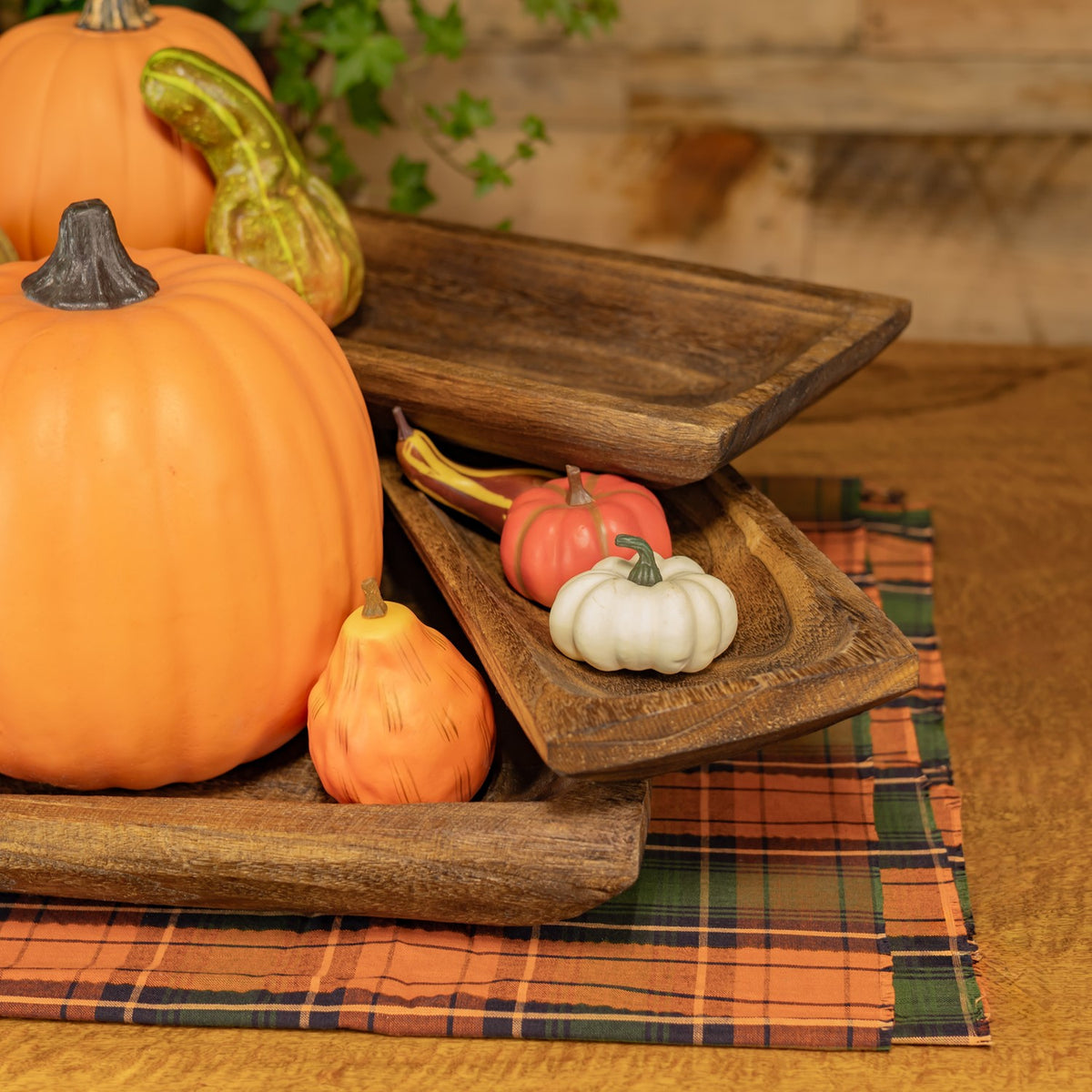 Rustic rectangular wooden trays arranged at angles beside pumpkins on an autumn plaid cloth.