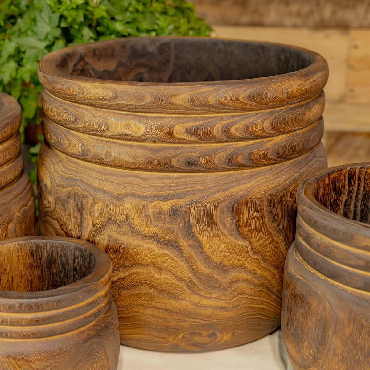 Large carved wooden bowl centered among several smaller bowls, showing swirling grain and ridged rims.