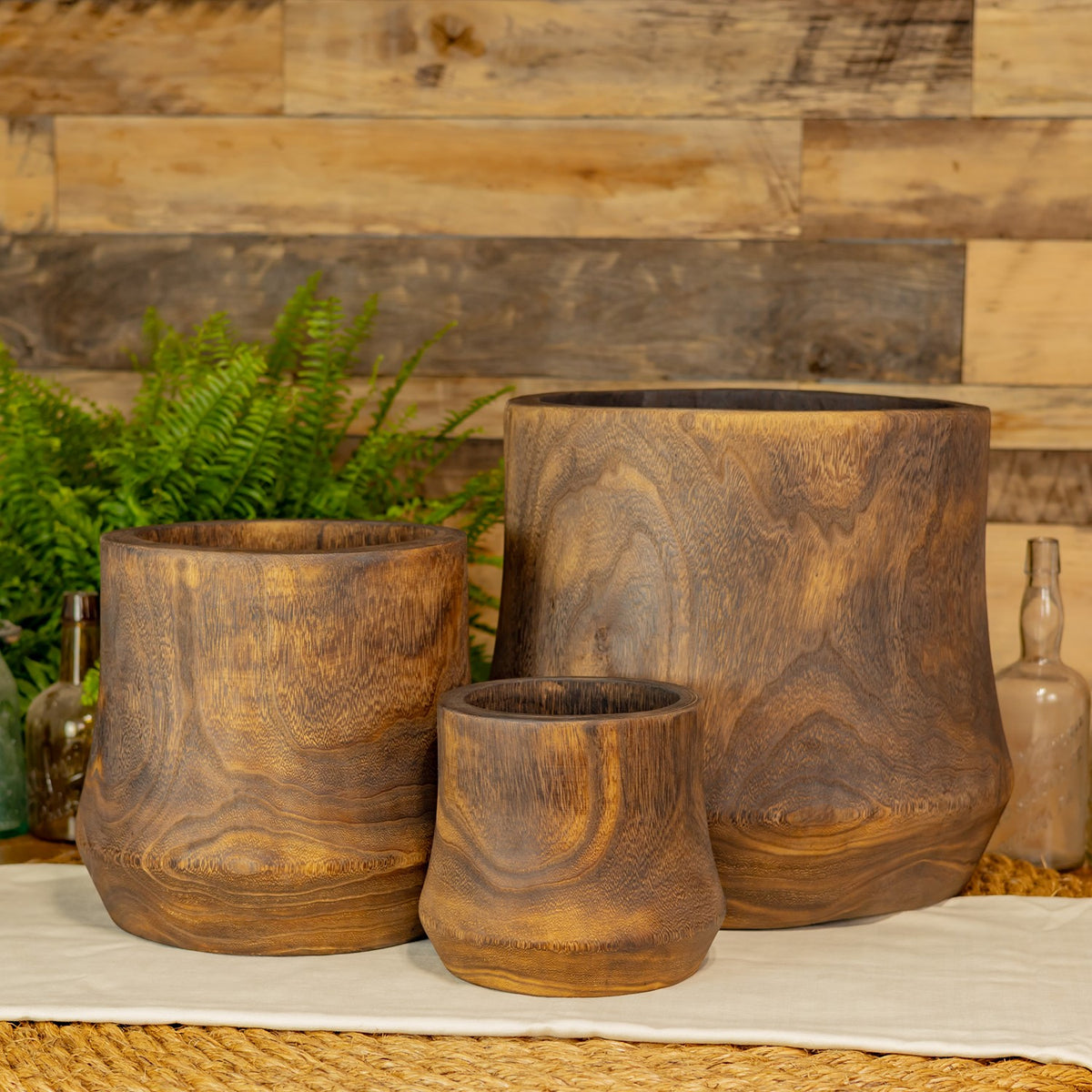 Three open, round wooden bowls in graduated sizes displayed together on a light cloth.