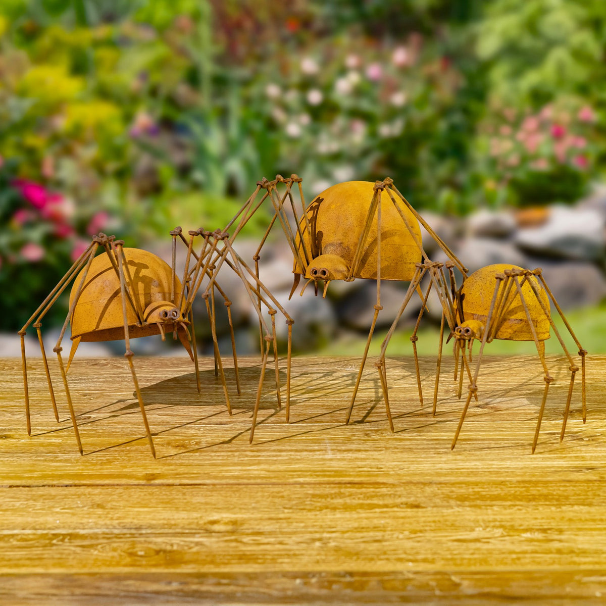 Three iron spider figurines arranged together on wood in a garden
