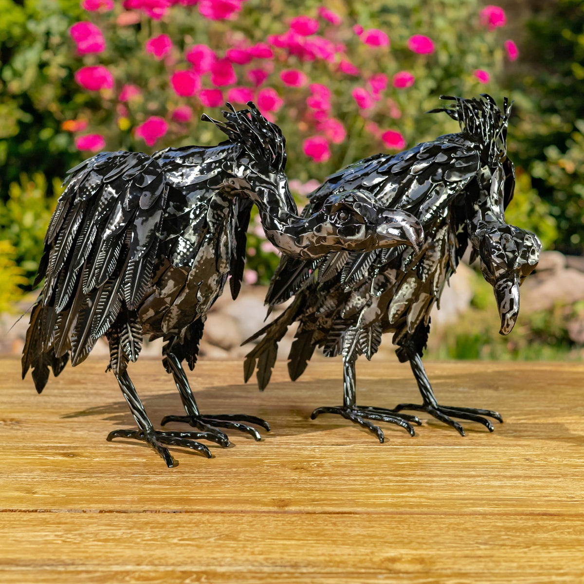 Two metallic black vulture figurines shown side by side on a wooden table