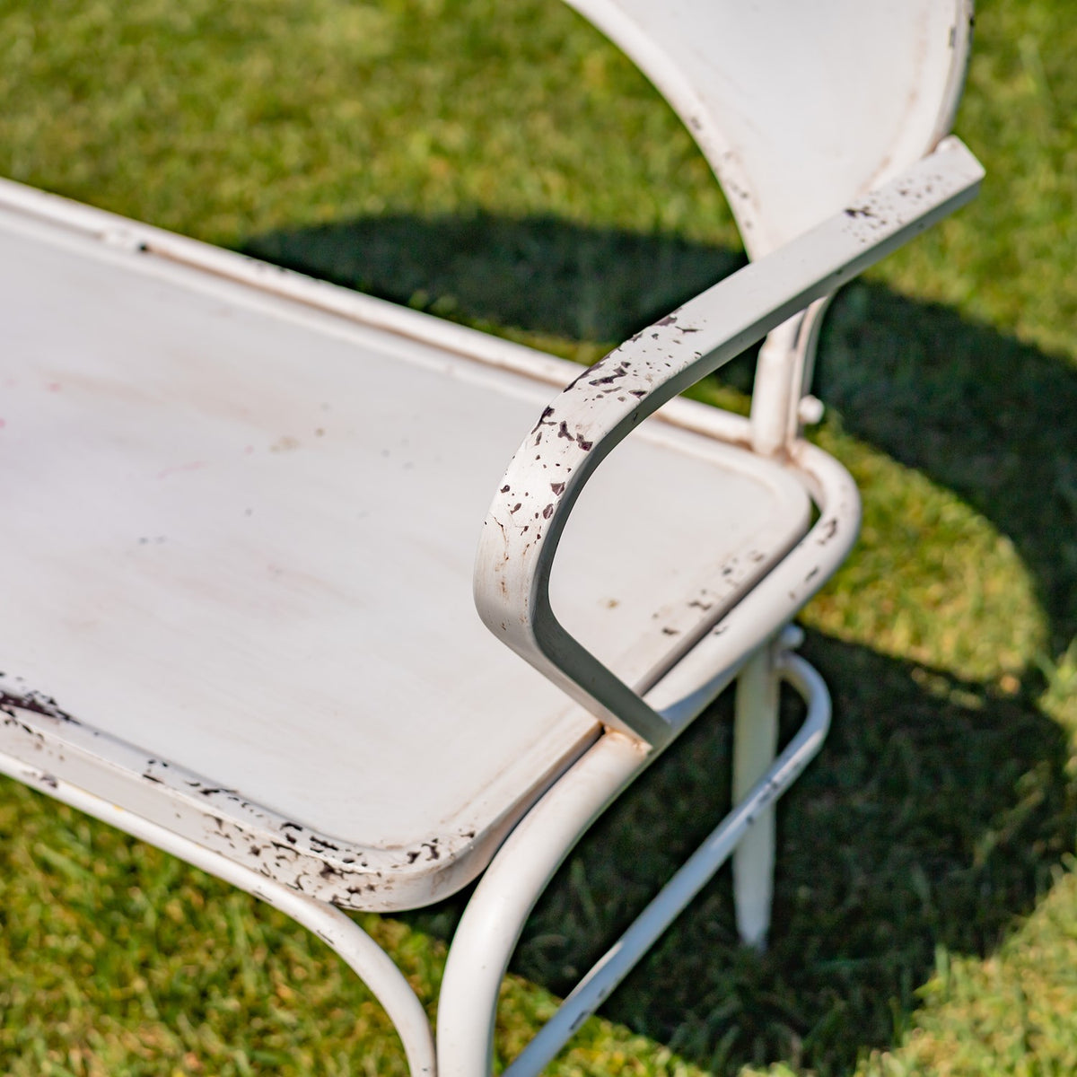 Close view of the white bench’s curved armrest, seat edge, and distressed finish.