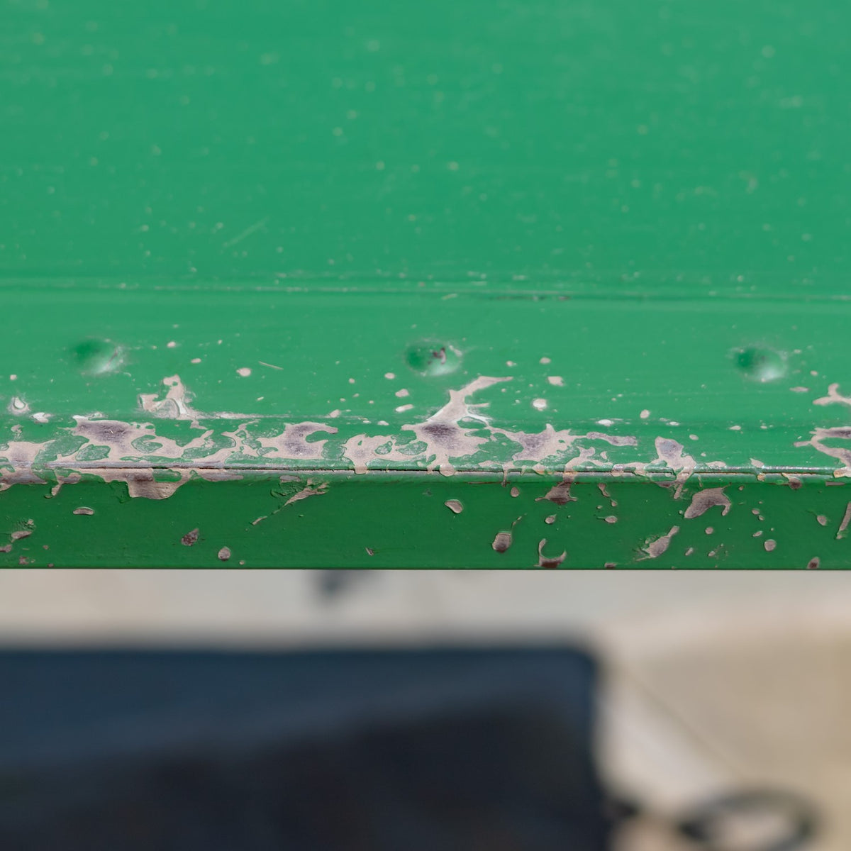 Close-up of a green tabletop edge with heavily chipped paint and exposed patches.