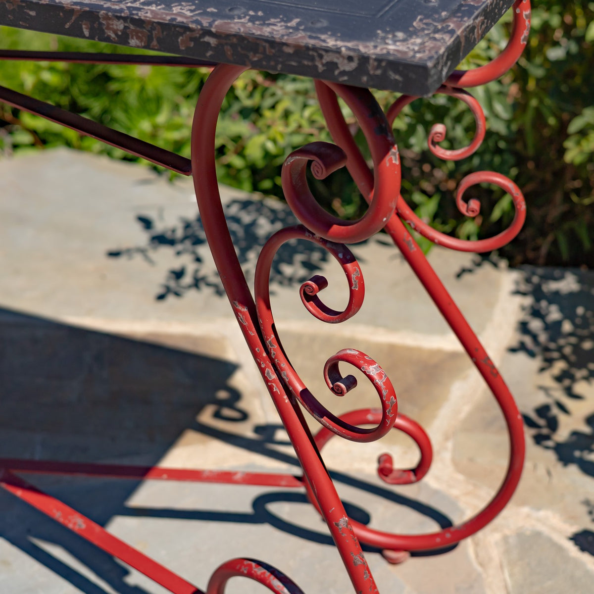 Angled close-up of the red iron table frame, showing curled metal supports and chipped finish beneath the top.