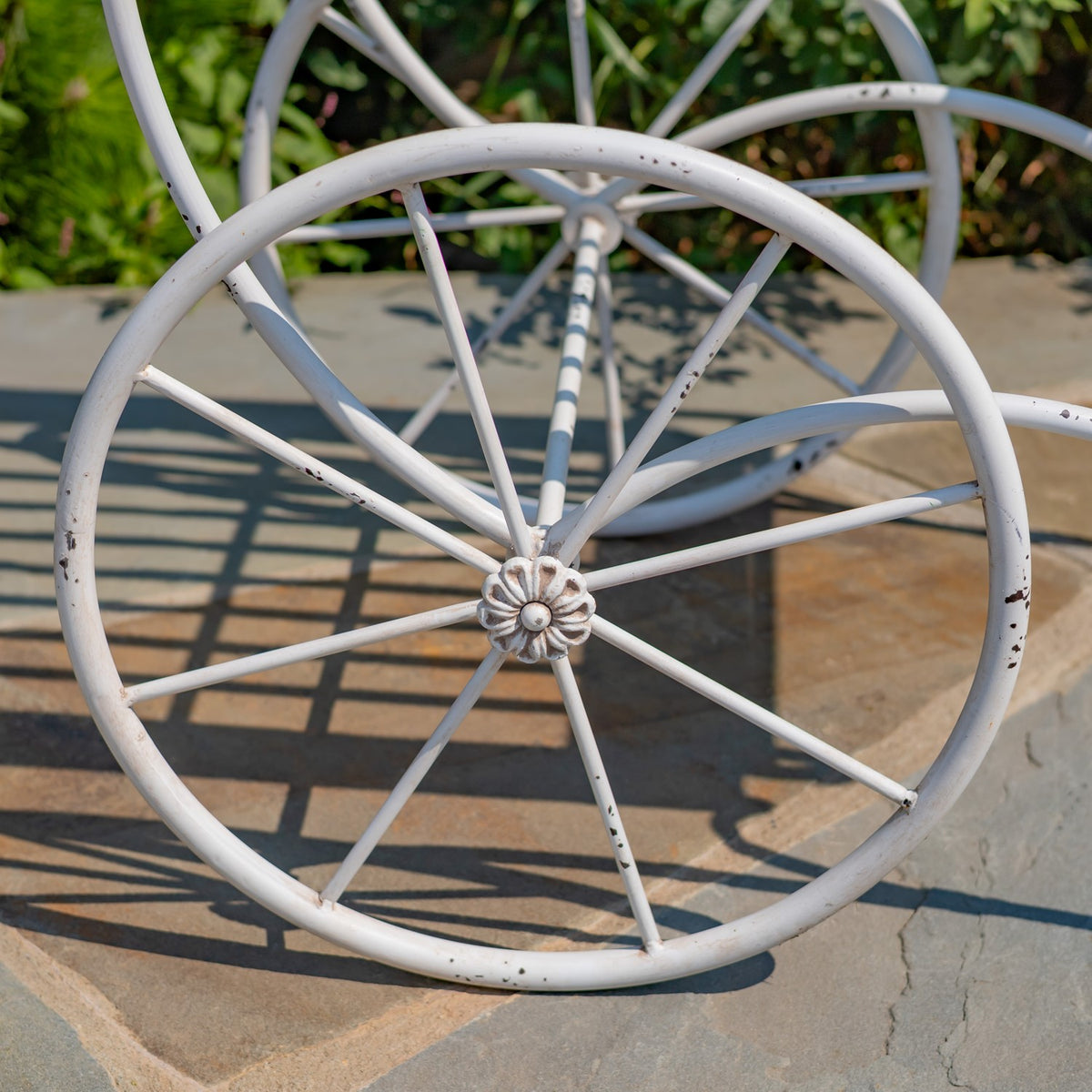 Close-up of a white spoked cart wheel with a flower-shaped center and chipped paint.