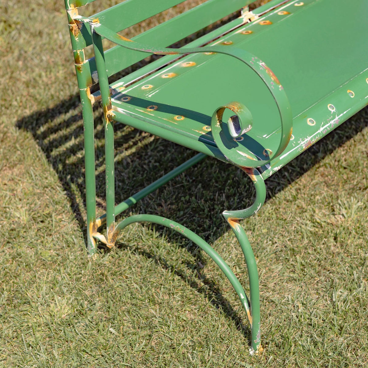 Close-up of a green metal bench arm and curved leg with worn paint and rust spots.
