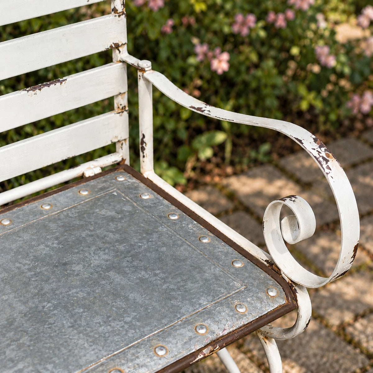Angled view of the bench’s gray metal seat and curled white arm, with worn paint.