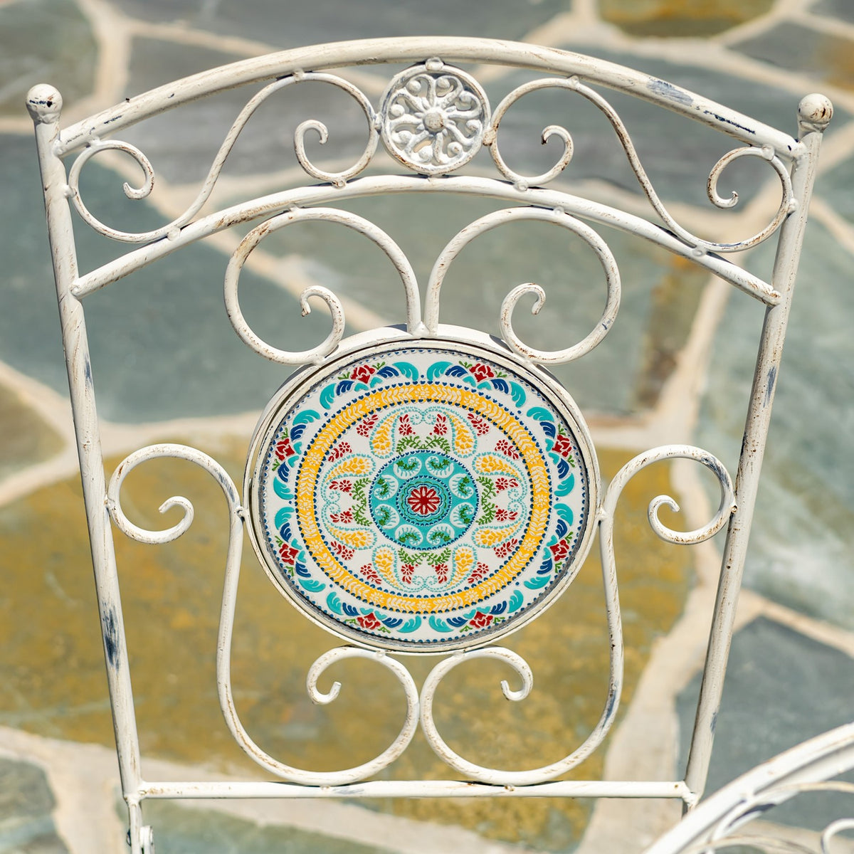 Antique-white metal chair back with ornate scrollwork and a colorful circular mosaic panel.