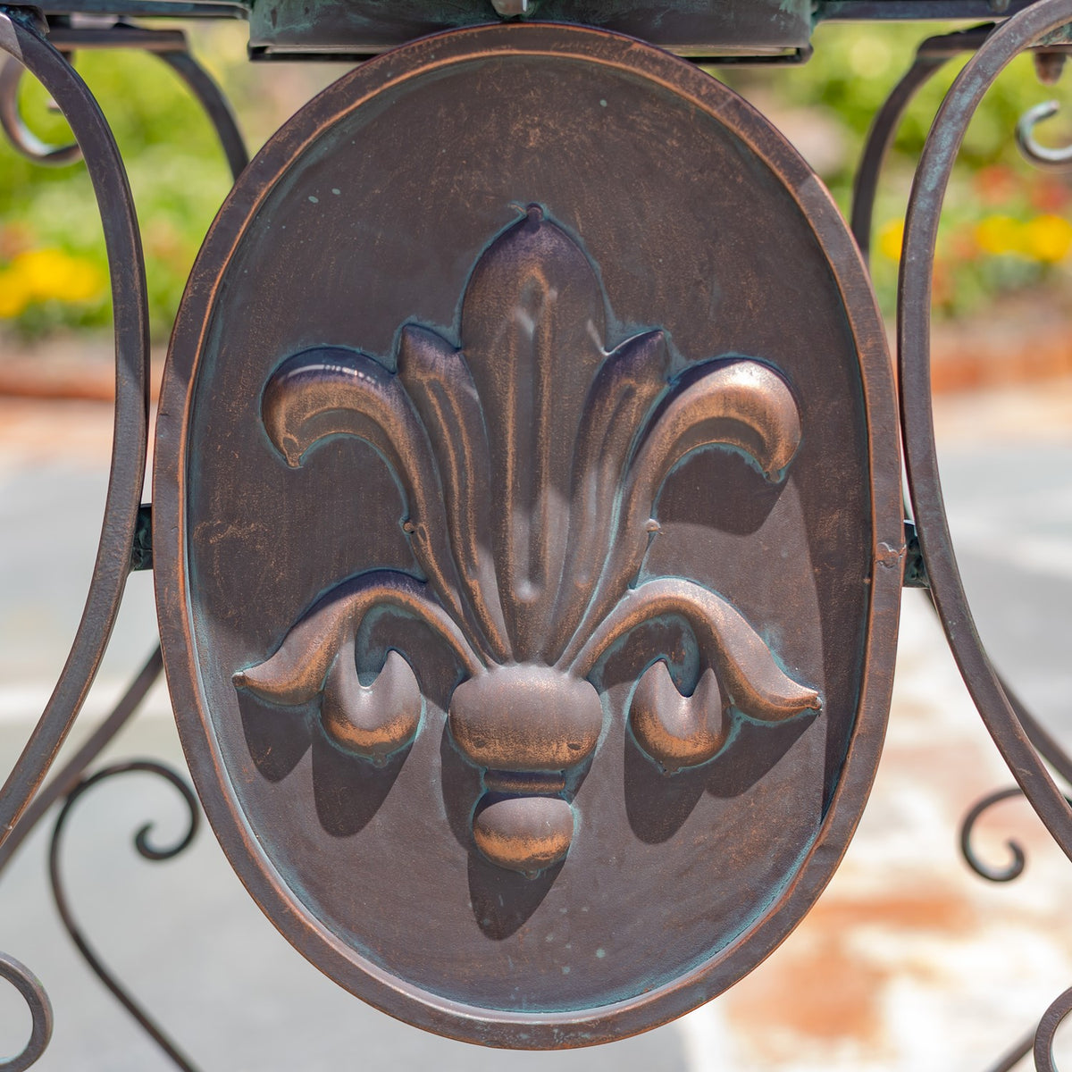 Close-up of an oval metal panel with a raised fleur-de-lis motif and curled ironwork.