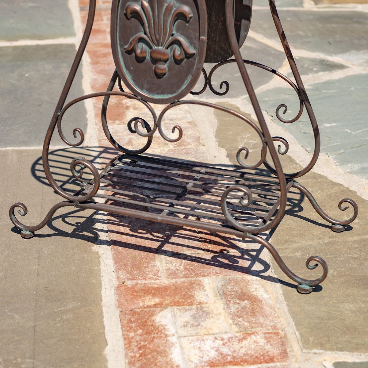 Curled metal legs and slatted lower shelf of a plant stand on a tiled patio.