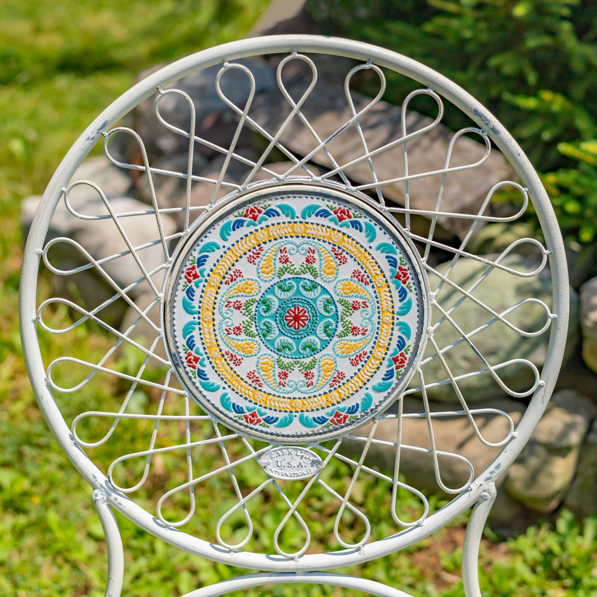 White wire-frame chair with a round, colorful floral-patterned back against a garden backdrop.
