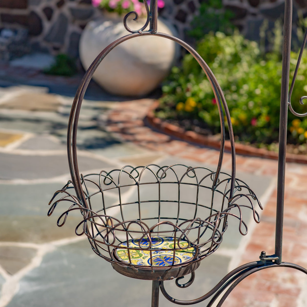 Close view of a dark metal wire basket with a colorful patterned base, set against a garden patio.