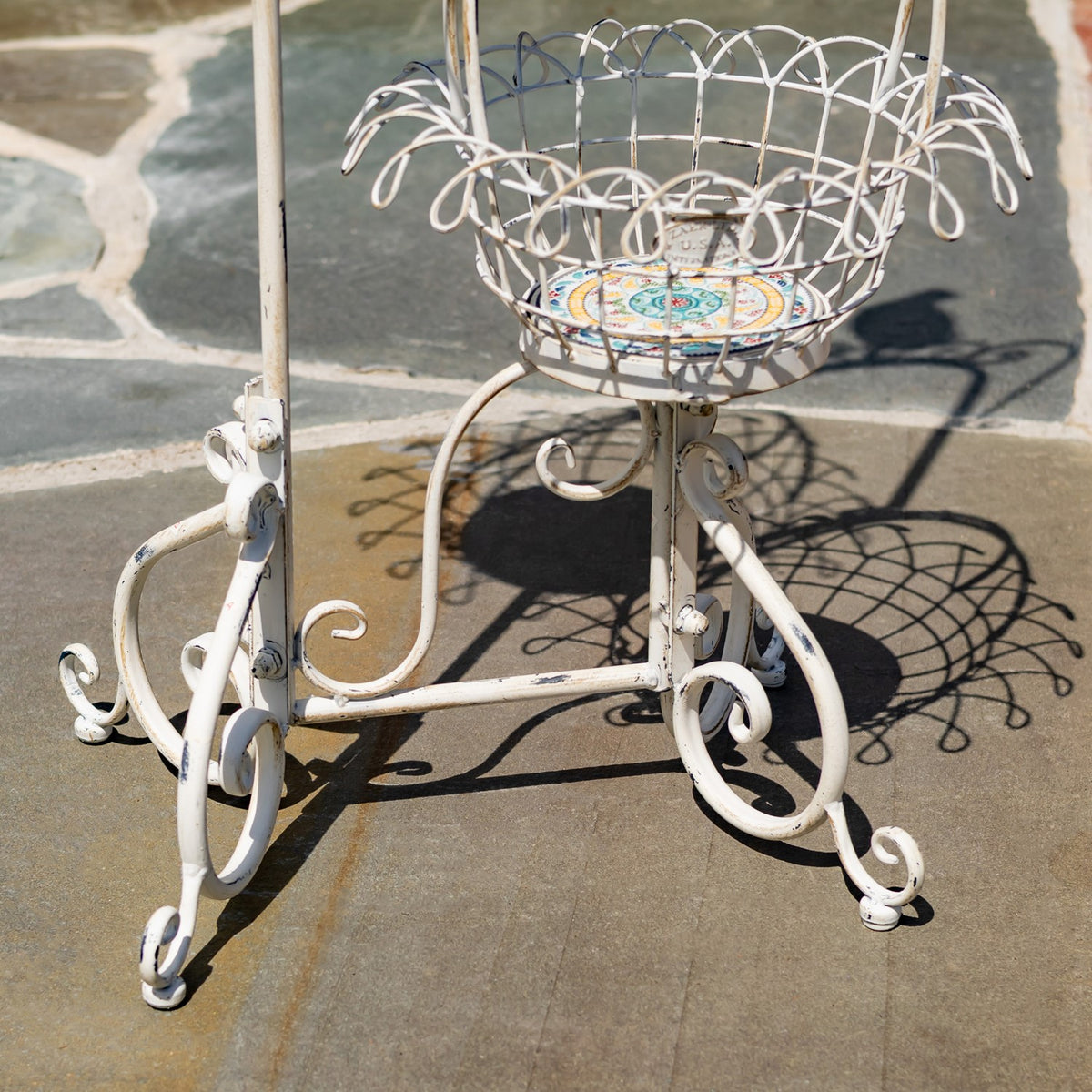 Lower portion of a white wire plant stand with curled metal legs and a colorful patterned basket base.