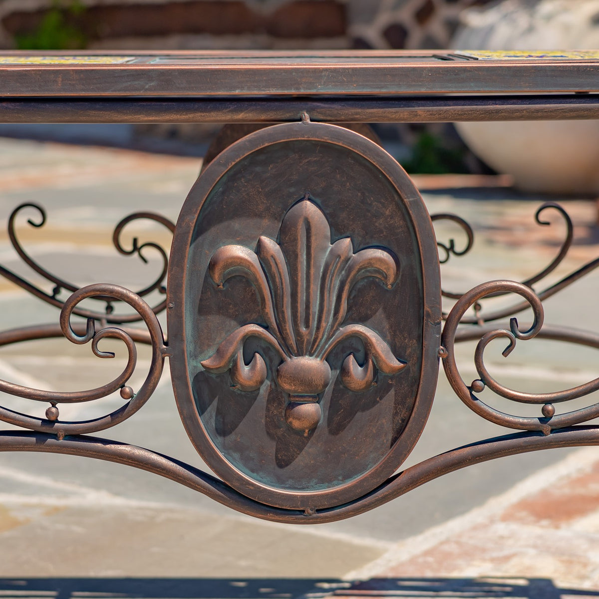 Close-up of the table’s metal base, showing a raised fleur-de-lis medallion and curled scrollwork.