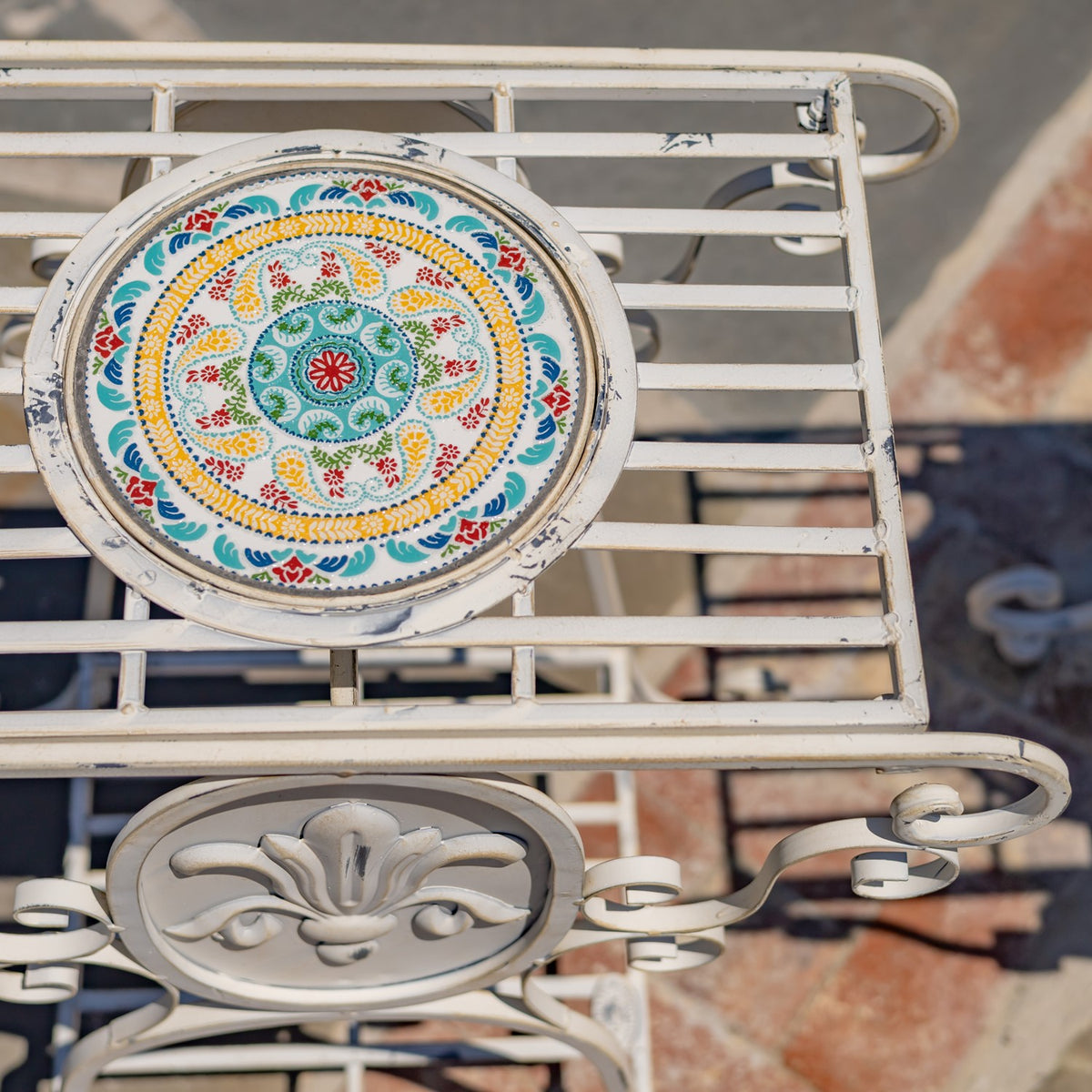 Close view of a colorful circular mosaic set into a pale metal table with slatted rails and scrollwork.