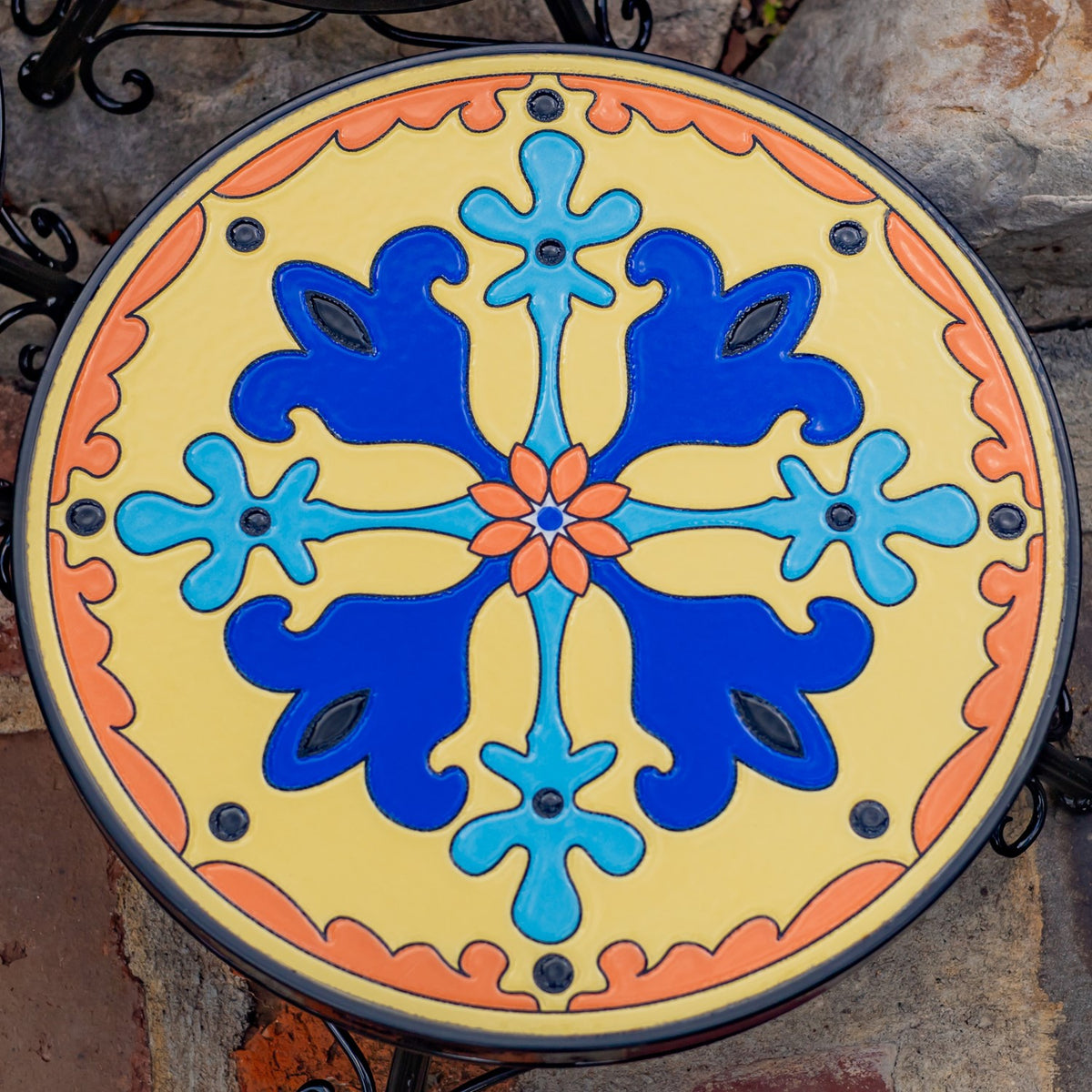 Close-up of a round plant stand top with a bright blue, turquoise, orange and yellow floral mosaic.