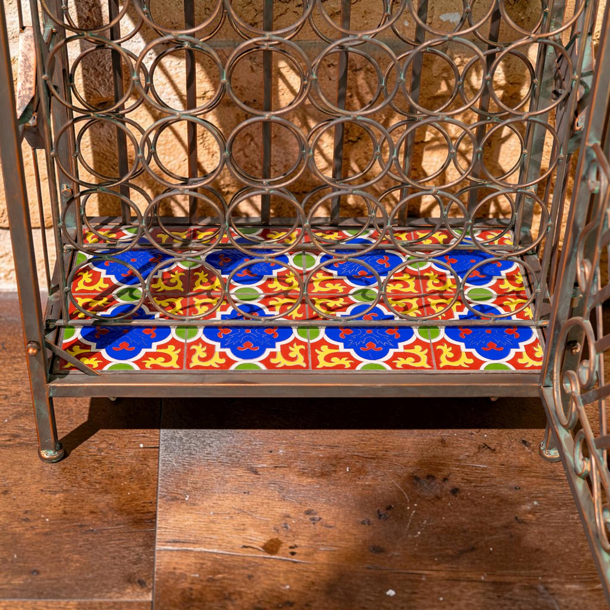 Lower section of an iron wine rack with circular bottle holders above a brightly patterned tile shelf.