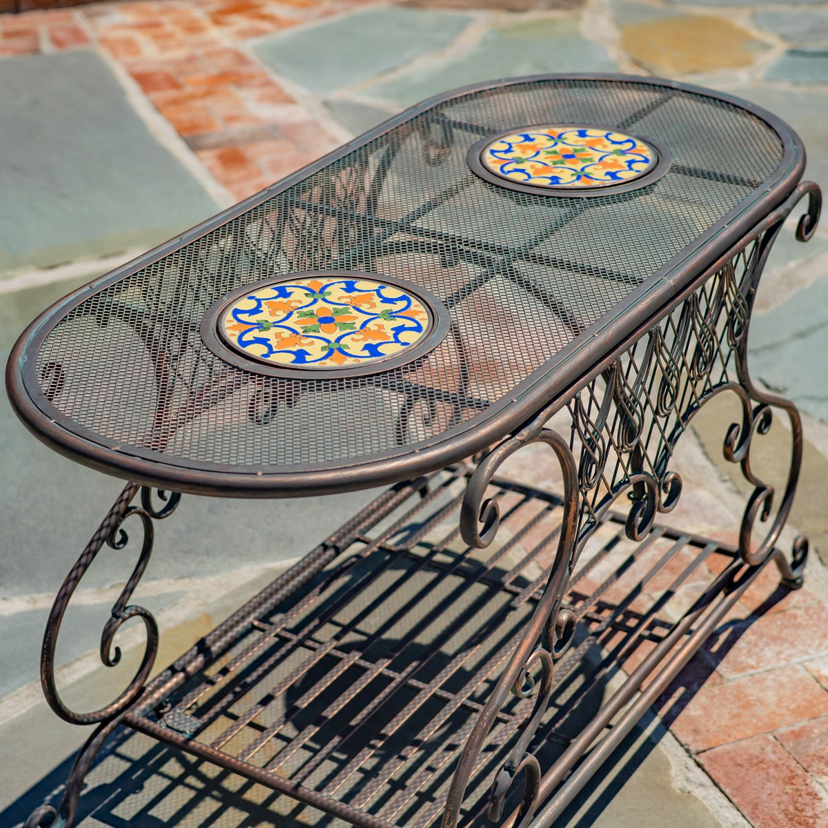 Oval metal garden table with two colorful mosaic insets and an ornate mesh shelf, viewed from above.