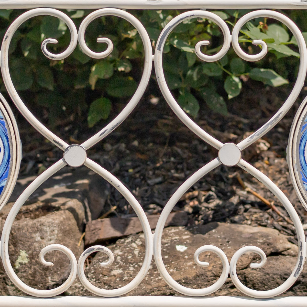 Close-up of a white metal bench panel with paired scrollwork and circular joints.