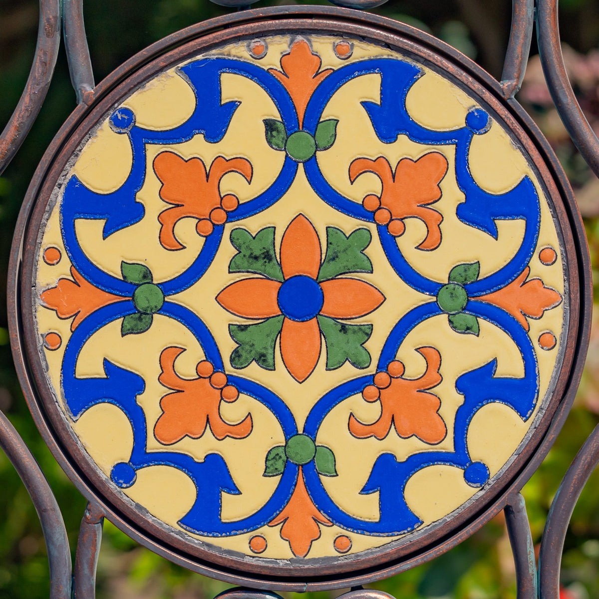 Close-up of a round floral mosaic tile with blue, yellow, orange, and green patterns in a bronze-colored metal frame.