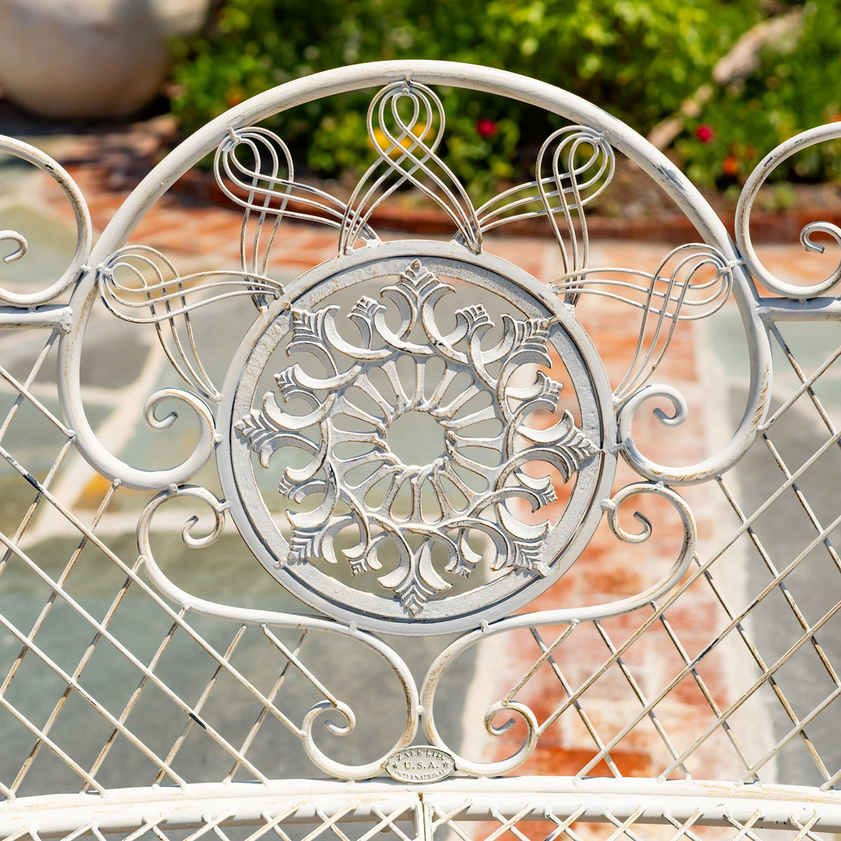 Close-up of the bench’s ornate white metal backrest medallion and curling scrollwork.