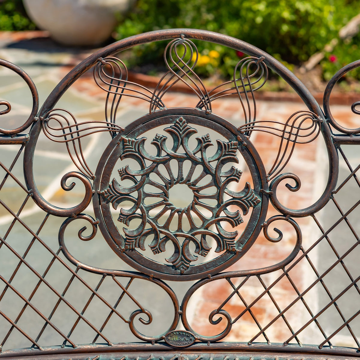 Close-up of the bench’s ornate dark metal backrest with a circular floral medallion and scrolling wirework.