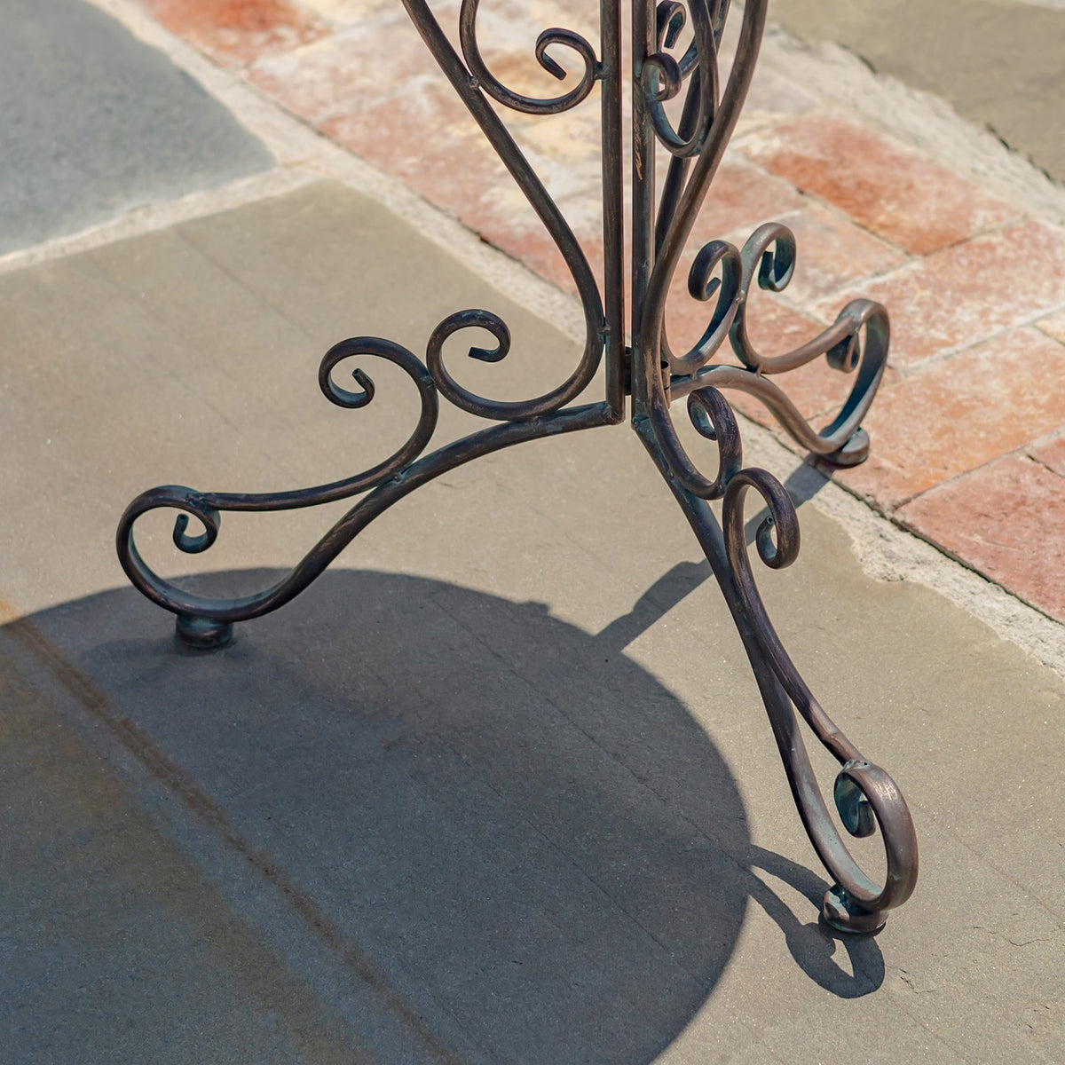 Curled dark metal legs and feet of the plant stand on a stone patio.