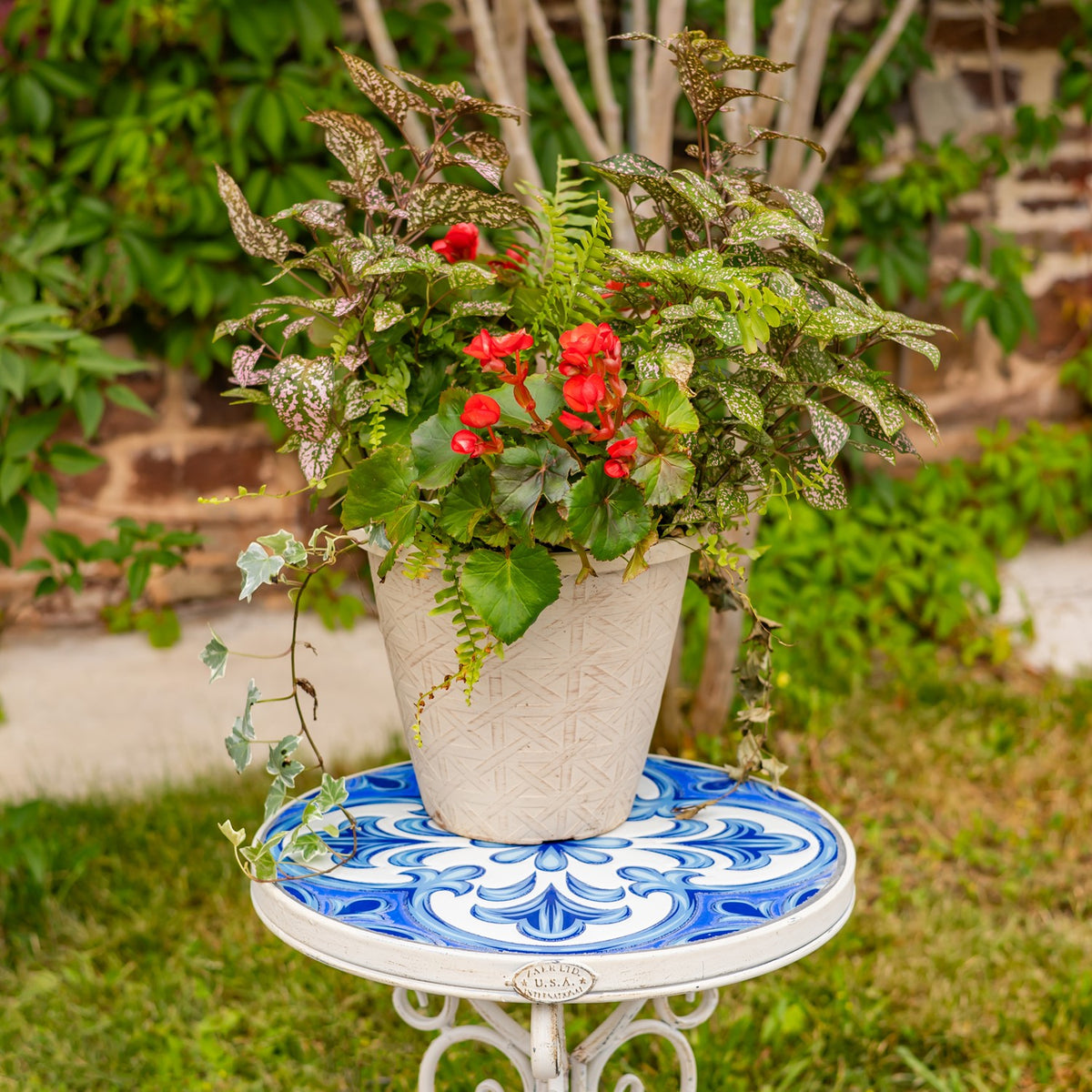 A potted arrangement of red flowers and greenery sits on a round blue-and-white mosaic stand.