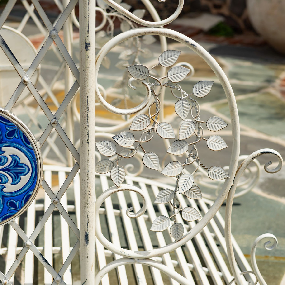 Close-up of pale metal bridge scrollwork with raised leaf ornaments and part of a blue mosaic medallion.