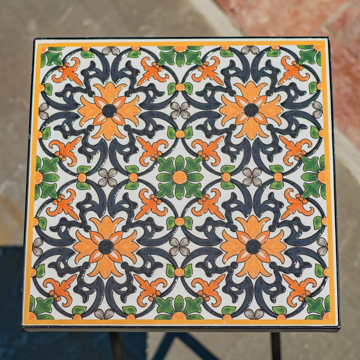 Square tabletop covered in a repeating floral mosaic in orange, green, gray, and black.