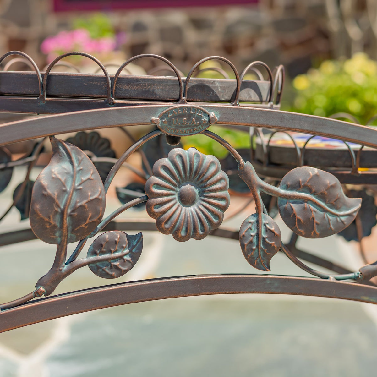 Close-up of the stand’s curved bronze-toned ironwork with a central flower and leaf ornaments.