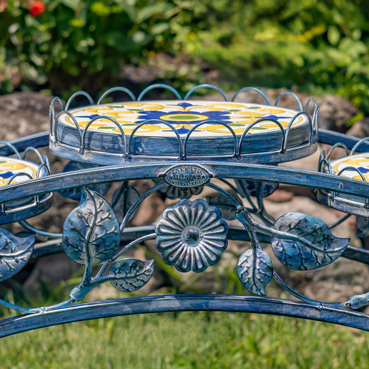 Close view of blue iron leaves and a flower ornament beneath a round mosaic tabletop.