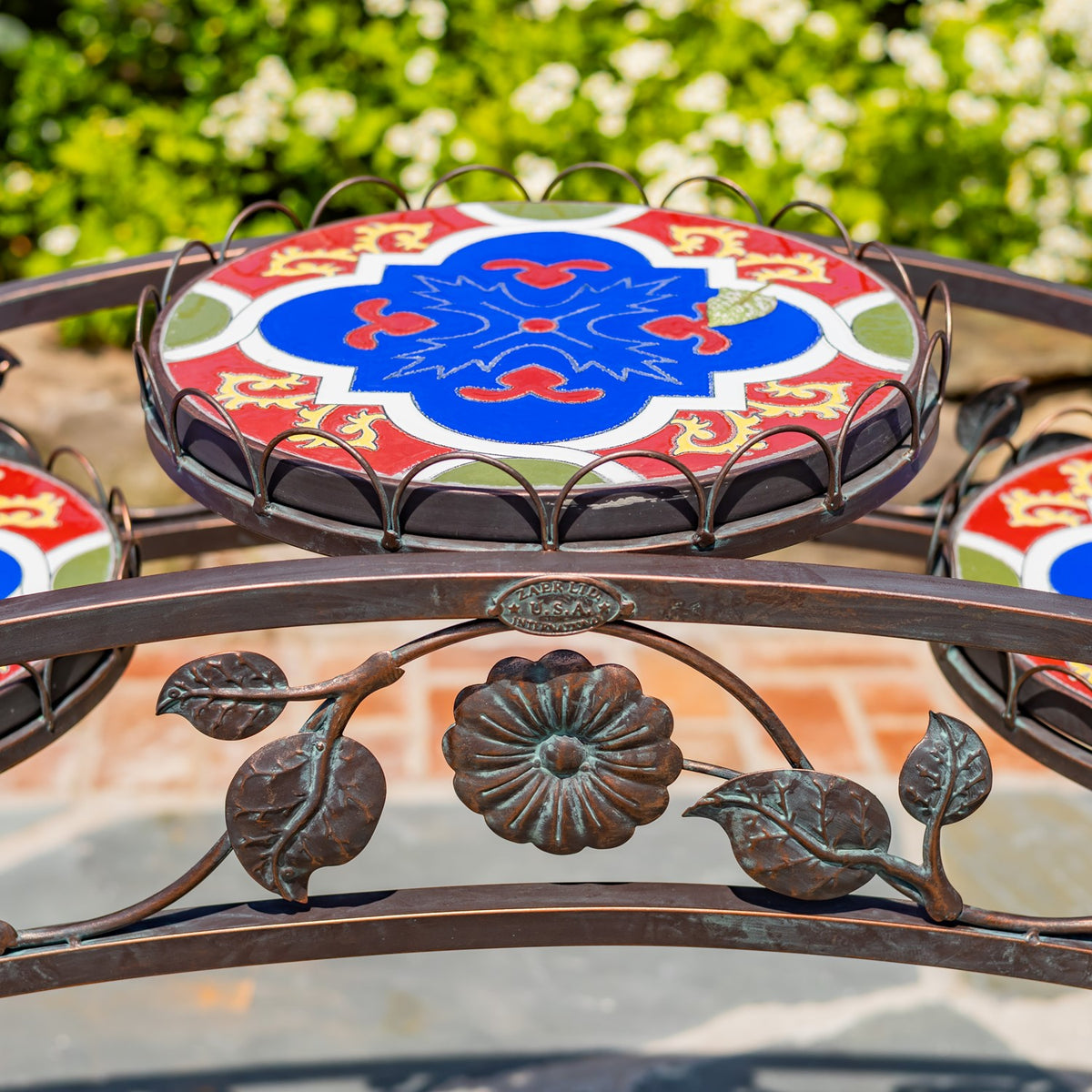 Colorful mosaic tabletop above an arched iron rail decorated with a metal flower and leaves.